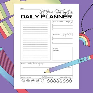 Puede incluir: Un planificador diario blanco con el texto "Get Your Shit Together" y "Daily Planner" en negro. El planificador incluye secciones para tareas, notas y un medidor de energía. Un lápiz con "Pride" está en el planificador.