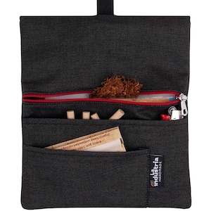 May include: Black canvas tobacco pouch with a red zipper, a small pocket, and the text "La Industria Handmade". The pouch is open and contains tobacco, rolling papers, and filters.