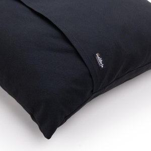 Puede incluir: Almohada negra con una costura negra en el centro y una peque&ntilde;a etiqueta naranja y negra que dice "industria handmade".