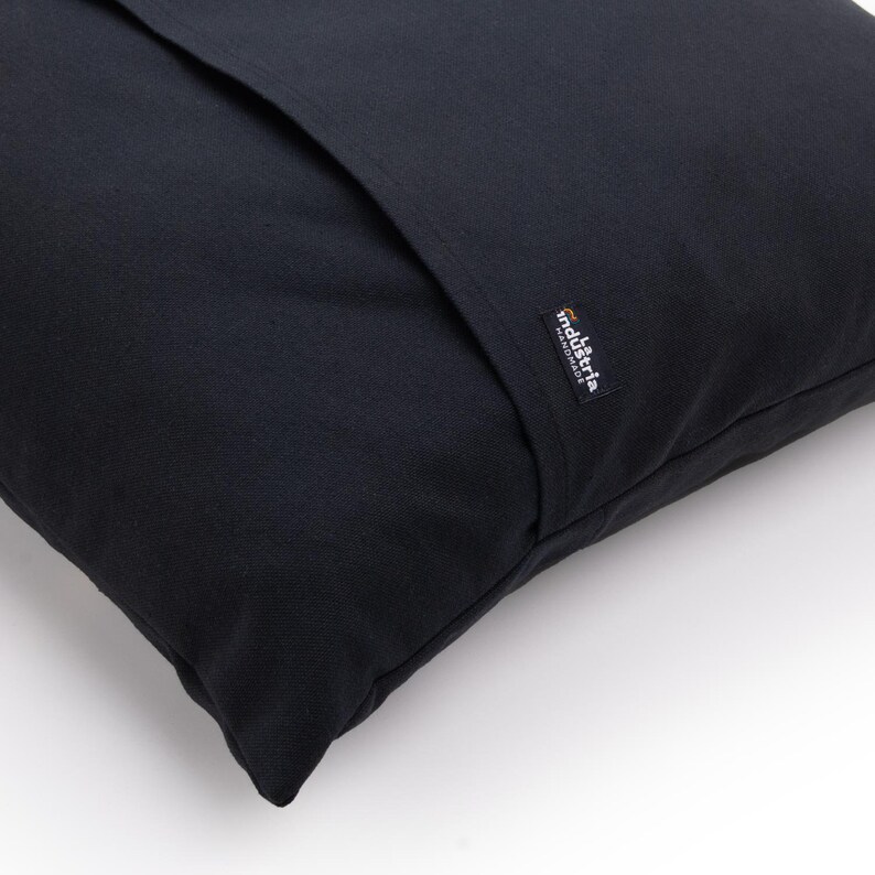 Puede incluir: Almohada negra con una costura negra en el centro y una peque&ntilde;a etiqueta naranja y negra que dice "industria handmade".