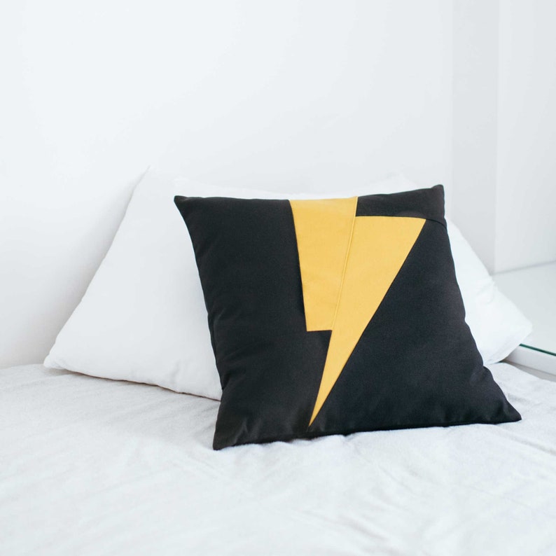 Puede incluir: Una almohada de tiro negra y amarilla con un dise&ntilde;o de rayo.