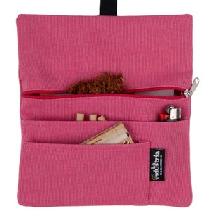 May include: A pink canvas tobacco pouch with a zipper closure. The pouch has multiple pockets and is labeled "La Industria Handmade".