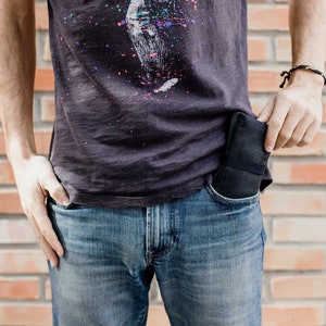 May include: A person wearing a dark grey t-shirt with a colorful splatter paint design and blue jeans. A black wallet is tucked into the front pocket of the jeans.