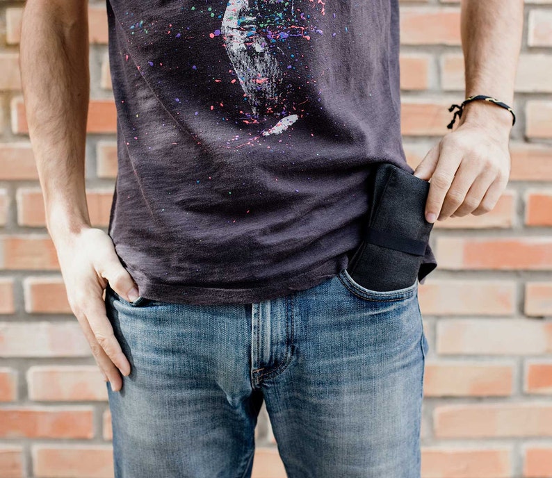 May include: A person wearing a dark grey t-shirt with a colorful splatter paint design and blue jeans. A black wallet is tucked into the front pocket of the jeans.
