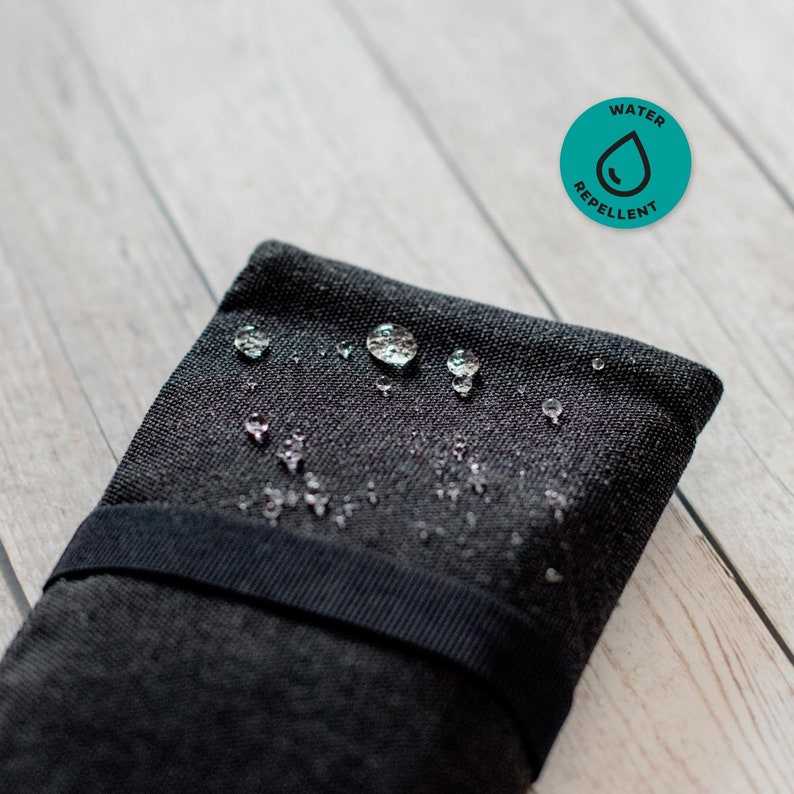 May include: A black fabric pouch with a black strap and water droplets on the surface. The pouch is water repellent, as indicated by the circular icon with the text "WATER REPELLENT" and a water droplet.