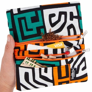 Puede incluir: Una bolsa de tela con múltiples compartimentos con un diseño geométrico en negro, blanco, naranja y verde. La bolsa contiene tabaco, un encendedor, una tarjeta de crédito y otros objetos pequeños.