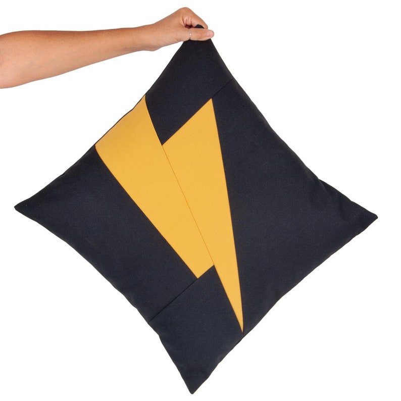 Puede incluir: Una almohada de tiro con estampado geom&eacute;trico negro y amarillo. La almohada est&aacute; hecha de una tela suave y texturizada.