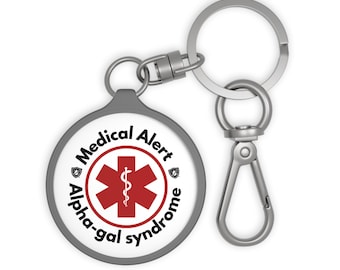 May include: A round, grey medical alert keyring with a silver clasp and key ring. The white face has a red medical symbol and the words "Medical Alert" and "Alpha-gal syndrome" in black text.