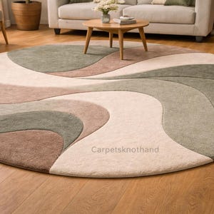 May include: A circular rug with a flowing, abstract pattern in shades of beige, brown, and green. The rug's design creates a sense of movement and adds a touch of elegance to the room. It is placed on a wooden floor, complementing the overall decor.