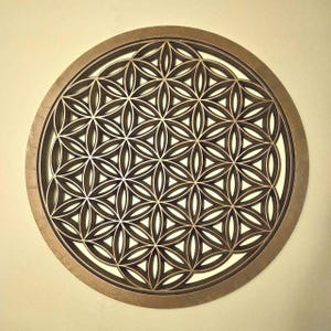 May include: A circular wooden wall art piece with a layered Flower of Life design. The artwork has a dark brown finish with a lighter brown interior, creating a 3D effect. The design is centered within a circular frame, suitable for home decor.