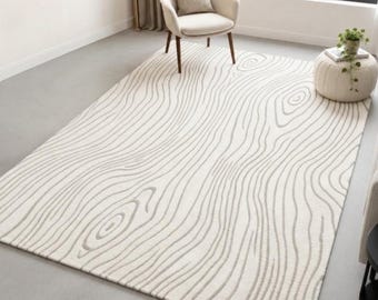 May include: A rectangular area rug featuring a cream-colored base with a repeating pattern of thin, wavy gray lines that mimic the organic, swirling texture of wood grain. The rug covers a large portion of the floor in a bright, open room.