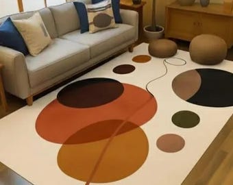 May include: A modern living room rug with an abstract design. The rug features overlapping circles in shades of orange, brown, and black against a white background. A gray sofa with blue and beige pillows sits above the rug.