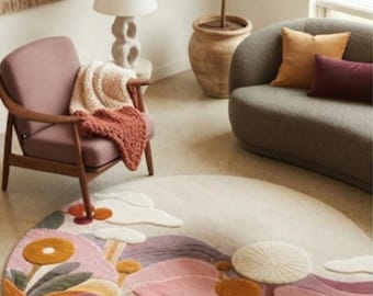 May include: A round area rug featuring a tufted landscape design with stylized flowers, rolling hills, and clouds in shades of cream, dusty pink, mustard yellow, sage green, and deep burgundy, creating a textured, multi-layered botanical scene.