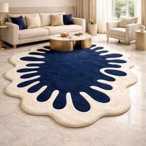 Puede incluir: Una alfombra grande, de forma única, con un centro azul marino y un borde crema irregular. El diseño de la alfombra presenta un patrón similar a una salpicadura, añadiendo un toque moderno al salón. La alfombra está colocada sobre un suelo de mármol.