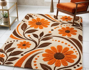 May include: A rectangular area rug featuring a cream-colored background with a repeating pattern of large orange daisy-like flowers and dark brown leaves. The design includes curved lines and small orange dots that flow across the surface.
