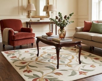May include: A rectangular area rug featuring a cream-colored background with a symmetrical floral pattern in shades of muted green, terracotta, and gold. The rug is positioned on a dark wood floor beneath a dark wood coffee table in a room.