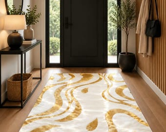 May include: A rectangular area rug featuring a white base with flowing, abstract gold-colored patterns. The rug is positioned on a wooden floor in an entryway, centered in front of a black door with glass side panels and a black console table.