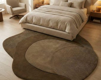 May include: A bedroom scene featuring a bed with beige bedding and pillows. A large, abstract-shaped rug in shades of brown sits on the wooden floor. A neutral-toned armchair and side tables with lamps complete the room's decor.