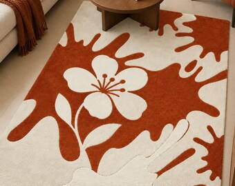 May include: A rectangular area rug featuring a high-contrast pattern of burnt orange and cream white. The design consists of large, fluid, organic shapes resembling liquid splashes, with a central five-petaled flower and leaves.