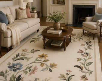 May include: A large rectangular area rug with a cream-colored background featuring a decorative floral border pattern. The design includes stylized flowers and leaves in shades of blue, yellow, green, and muted pink, arranged along the edges.