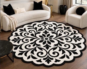 May include: A round area rug featuring a high-contrast black and white floral damask pattern with a scalloped edge. The design consists of symmetrical, swirling leaf and petal motifs radiating from a central flower shape on a white background.