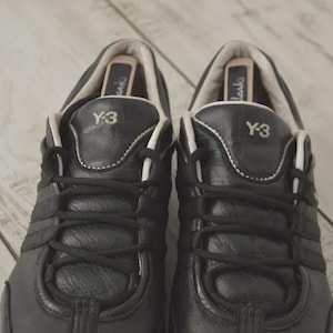 May include: Pair of black leather Y-3 sneakers with white accents and laces. The Y-3 logo is visible on the tongue. The shoes have a classic athletic design.