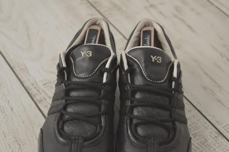 May include: Pair of black leather Y-3 sneakers with white accents and laces. The Y-3 logo is visible on the tongue. The shoes have a classic athletic design.