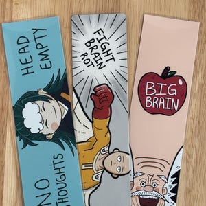 May include: Three colorful bookmarks with cartoon illustrations and text. One bookmark has a character with the text "HEAD EMPTY NO THOUGHTS". Another has a superhero with the text "FIGHT BRAIN ROT". The last has an apple with the text "BIG BRAIN".