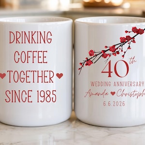 May include: A white ceramic mug with a black handle and the text "But First, Coffee" in a bold, black font. The mug is set against a blurred background, suggesting a cozy setting. The mug appears to be approximately 4 inches tall.