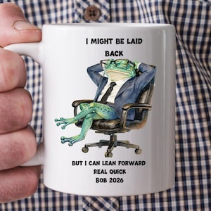 May include: White ceramic mug featuring a frog in a suit, wearing glasses, and sitting in an office chair. The mug has the text "I MIGHT BE LAID BACK BUT I CAN LEAN FORWARD REAL QUICK BOB 2026."