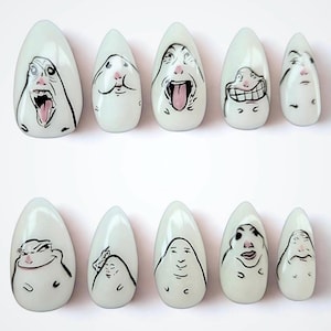 May include: A set of ten almond-shaped press-on nails with a glossy off-white finish. Each nail features a unique hand-drawn black ink illustration of a stylized face with distinct facial expressions, including wide mouths, grins, and neutral looks.