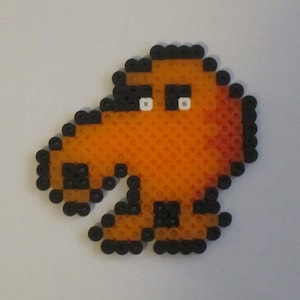 May include: A pixel art character made of black and orange beads. The character is shaped like a bird with a long beak and large eyes.