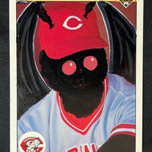 May include: A baseball card featuring a stylized illustration of a moth-like creature wearing a Cincinnati Reds baseball cap and jersey. The word "Mothy" is written in yellow at the bottom of the card.