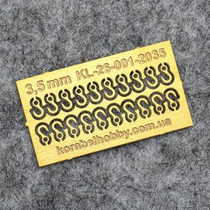 May include: A small, rectangular brass piece with multiple hook-shaped cutouts. The text "3,5 mm KL-26-001-2035" and "korabelhobby.com.ua" are printed on the brass. The background is a textured gray surface.