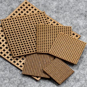 May include: A selection of laser-cut wooden squares and rectangles featuring a woven design. The pieces are of varying sizes, with the largest measuring about 15 cm by 15 cm. The wood has a natural, light brown hue.