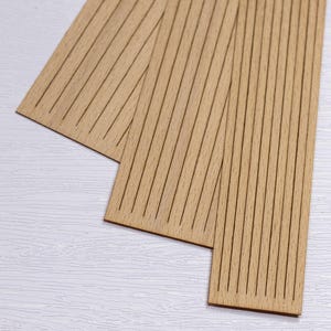 May include: Three rectangular wooden panels with parallel grooves. The panels are light brown and arranged on a white surface. The grooves are dark brown and run the length of each panel.
