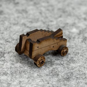 May include: A miniature wooden catapult toy with a detailed design. The catapult has a brown finish, with small wheels and a stepped structure. The toy is designed to resemble a historical siege weapon.