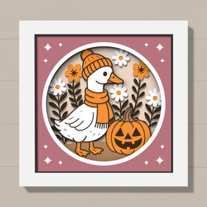 May include: A framed, layered paper art piece featuring a white goose wearing an orange hat and scarf, with a carved pumpkin and flowers. The background is a dusty rose color with white stars. The artwork is in a white frame.