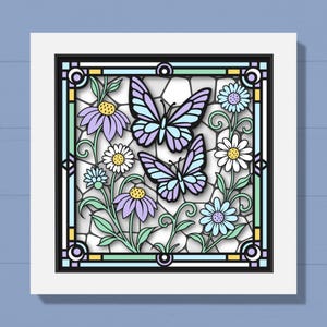 May include: A framed artwork featuring a stained-glass design with two butterflies and various flowers. The butterflies have light blue and purple wings, and the flowers are in shades of purple, white, and blue. The frame is white with a black border.