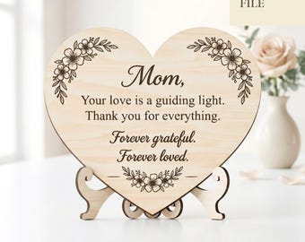Peut inclure: Un panneau en forme de cœur en bois avec le mot "Maman" et un message affectueux, soutenu par un support en bois. Le panneau est orné de motifs floraux et du texte "Laser Cut File" et "Digital Download".
