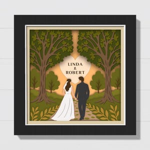May include: A framed paper cut art piece featuring a bride and groom walking hand-in-hand on a path. The artwork includes trees, foliage, and the names "LINDA & ROBERT" inside a heart shape. The frame is black.
