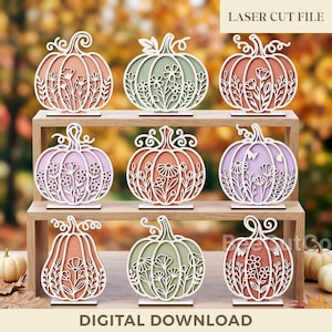 May include: A collection of nine laser-cut pumpkin decorations arranged on a two-tiered wooden stand. Each pumpkin features intricate floral cutouts in various pastel colors including peach, sage green, and lavender. Text reads LASER CUT FILE.
