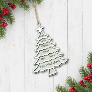 May include: A light gray wooden Christmas tree ornament with a star on top and the year 2025. The ornament is engraved with names and the family name "THE WILLIAMS". It hangs from a natural twine string.
