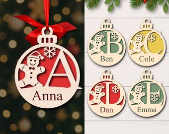 May include: Wooden Christmas ornaments with a gingerbread man design. One ornament has the letter "A" and the name "Anna". Other ornaments have the letters B, C, D, and E with names. Each ornament has a red or yellow background. A red ribbon is attached to the ornament.