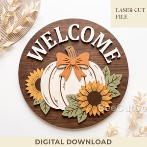May include: A circular wooden sign featuring the white text WELCOME at the top. The centre displays a light-coloured pumpkin with an orange bow, flanked by two yellow sunflowers and green leaves. The text LASER CUT FILE and DIGITAL DOWNLOAD appear.