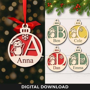 Könnte beinhalten: Weihnachtsschmuck aus Holz mit Pinguin-Design und personalisierten Buchstaben. Die Ornamente sind rund mit rotem Hintergrund und natürlicher Holzoberfläche. Ein Ornament hängt mit einem roten Band. Der Text "Anna" ist sichtbar.