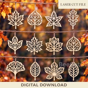 Peut inclure: Une collection de douze ornements en forme de feuilles en bois découpés au laser avec des motifs en filigrane complexes, suspendus à trois cordes horizontales. Le texte LASER CUT FILE et DIGITAL DOWNLOAD est visible sur l'image.