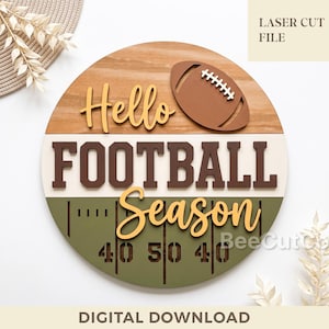 Könnte beinhalten: Ein rundes Holzschild mit dem Text Hello FOOTBALL Season in geschichteter Schrift. Das Design enthält ein braunes Football-Symbol und eine grüne Spielfeldgrafik mit Linienmarkierungen sowie den Zahlen 40, 50 und 40.