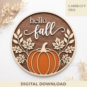 May include: A circular wooden wall sign featuring a dark brown wood grain background with a light-coloured frame. The sign displays the text hello fall in white script and block lettering above a large orange pumpkin and leafy branches.