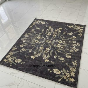 Peut inclure: Un tapis rectangulaire gris foncé avec un motif floral crème et vert clair. Le tapis présente un médaillon floral central et une bordure florale. Le texte "©Rugs Art Studio" est visible sur le tapis.